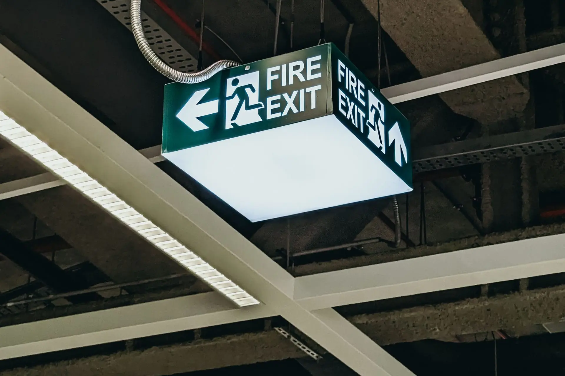 Tavandan sarkan yeşil "Fire Exit" acil çıkış yönlendirme levhası