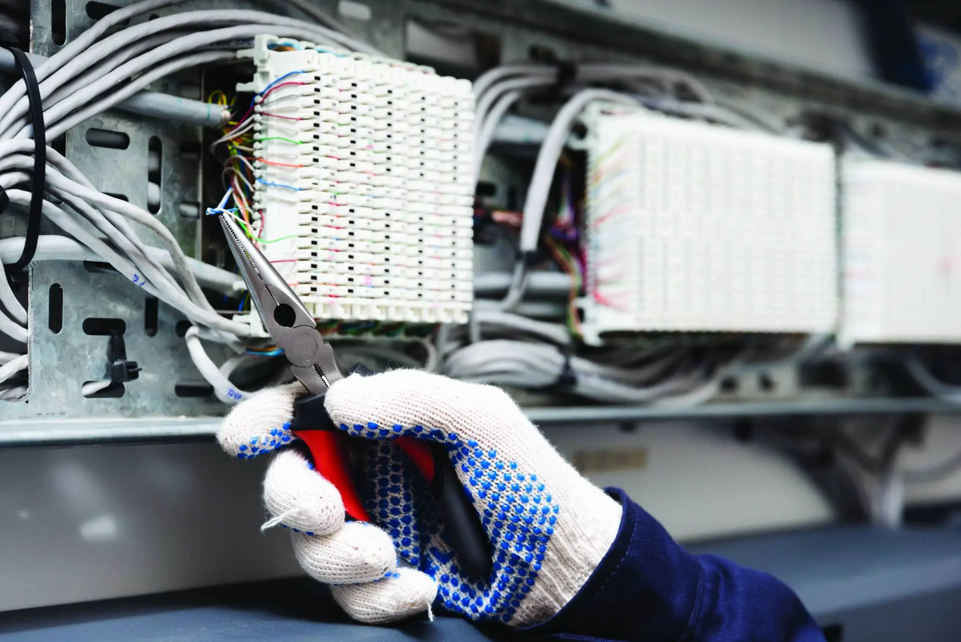 Pano içindeki kabloları ve klemensleri koruyucu eldivenle düzenleyen elektrik teknisyeni